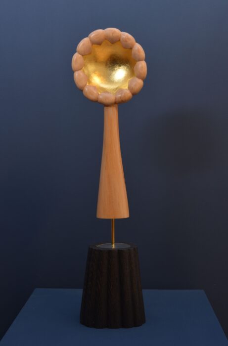 Carved basswood sculpture with gold leaf on a brass rod above a blackened oak base with mirror.