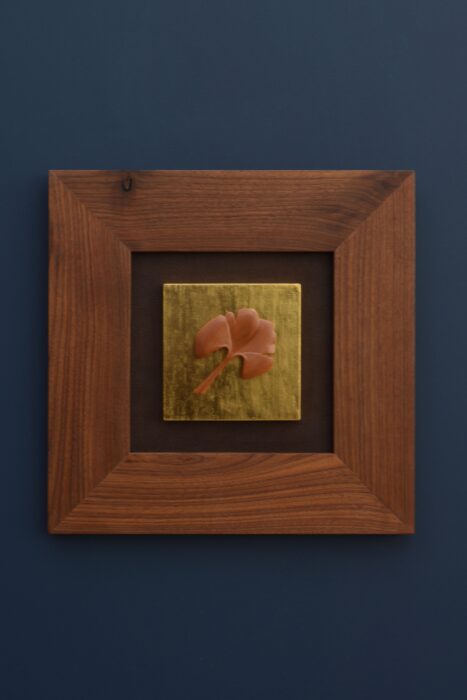 Delicate wooden ginkgo leaf floating over warm gold leaf, framed in walnut with a leather backing.